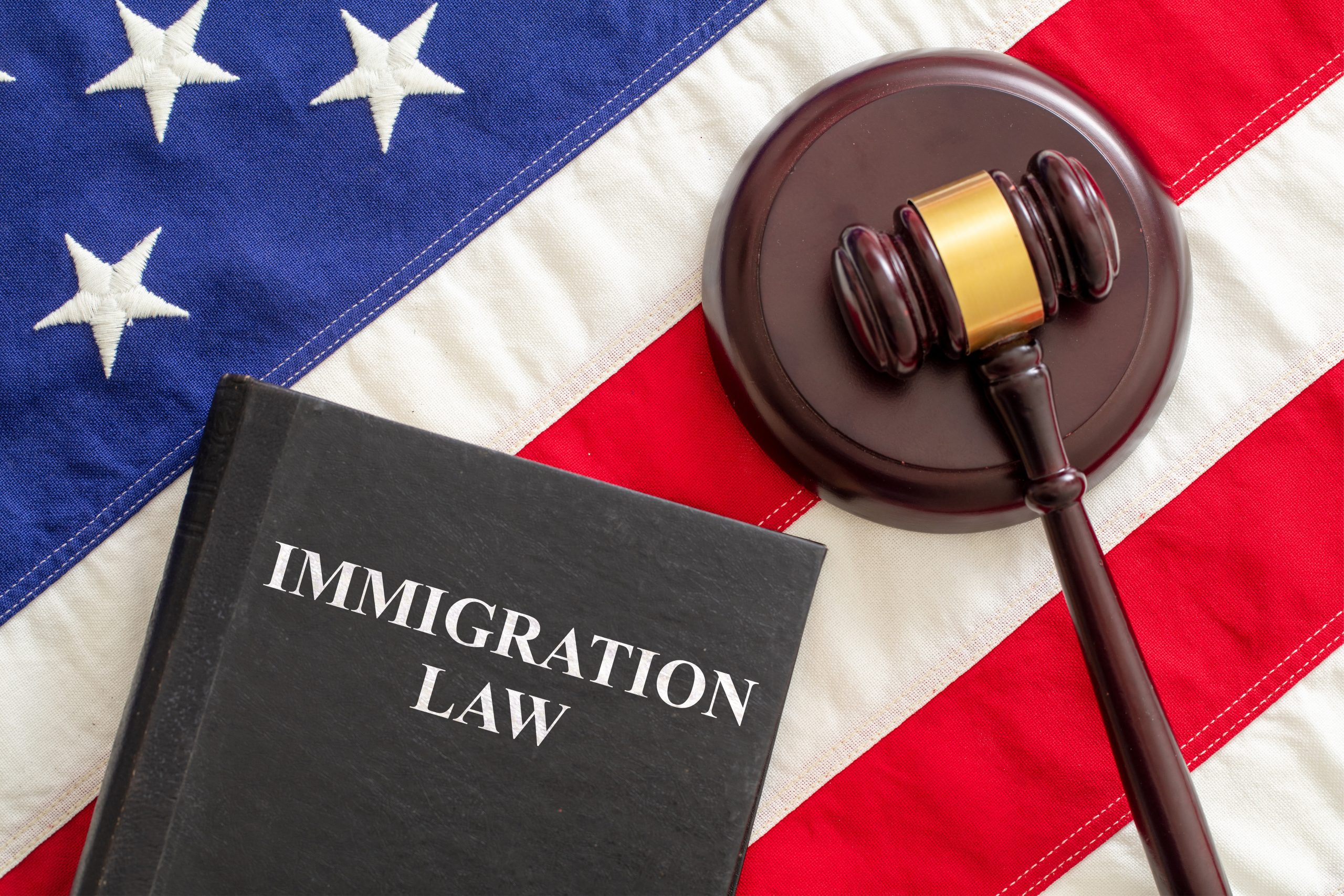 Judge gavel and Immigration Law book on United States of America flag. Immigration law text on black book and judge gavel on US of America flag background, top view. Migration, emigration visa in USA concept